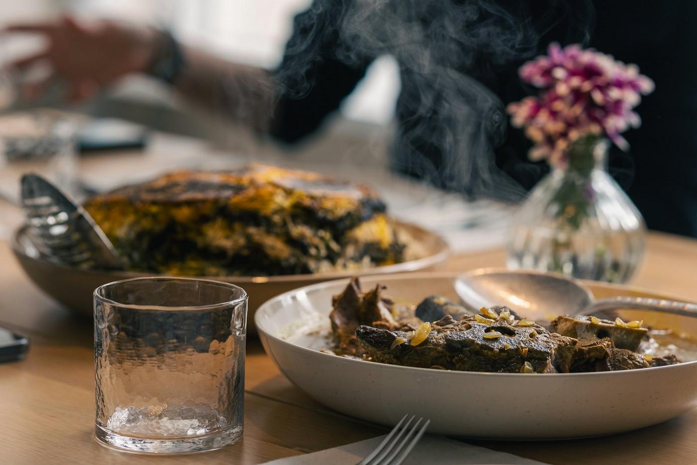 Pratos servidos ainda fumegando numa mesa de casa, com flores num vaso de vidro